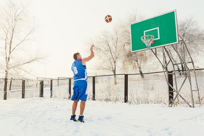basketball player in blue uniform throwing a basketball ball into the basket on a street basketball court in the winter