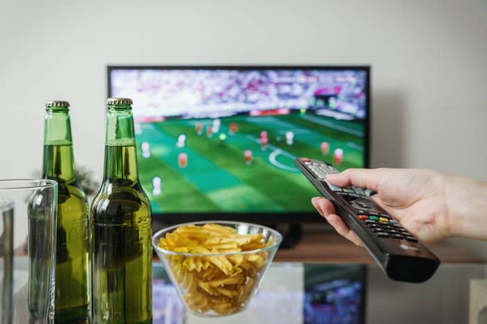 Person watching football on tv with a remote in his hand